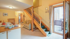 A spacious living area with a wooden staircase, a dining table set with dishes, and a sofa. - Genziana (Livigno)