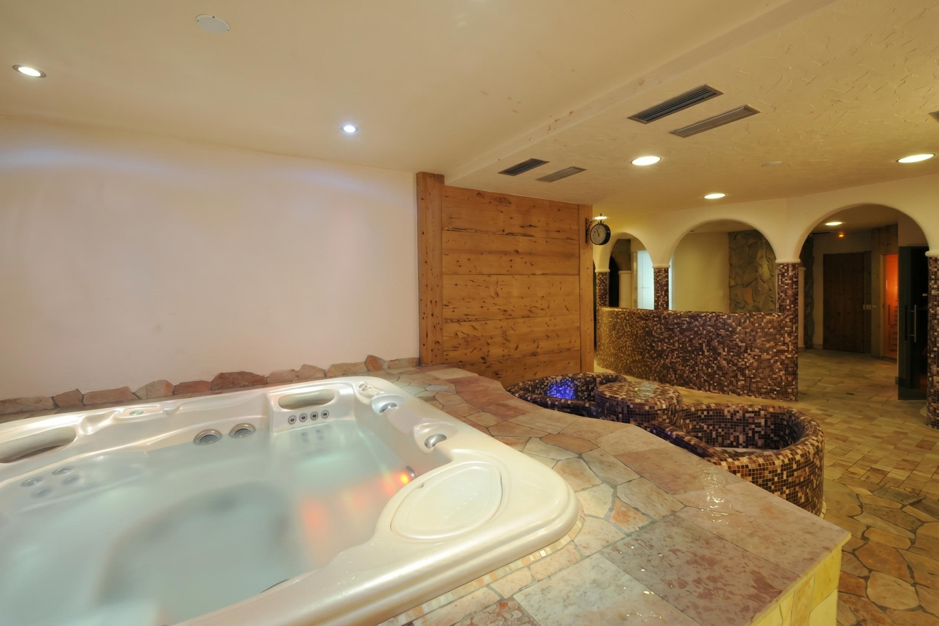 Un jacuzzi con borde de piedra, pared de madera y suelo de baldosas.