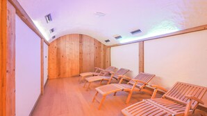 A room with wooden walls, a sloped ceiling, and several wooden lounge chairs arranged in rows. - Genziana (Livigno)