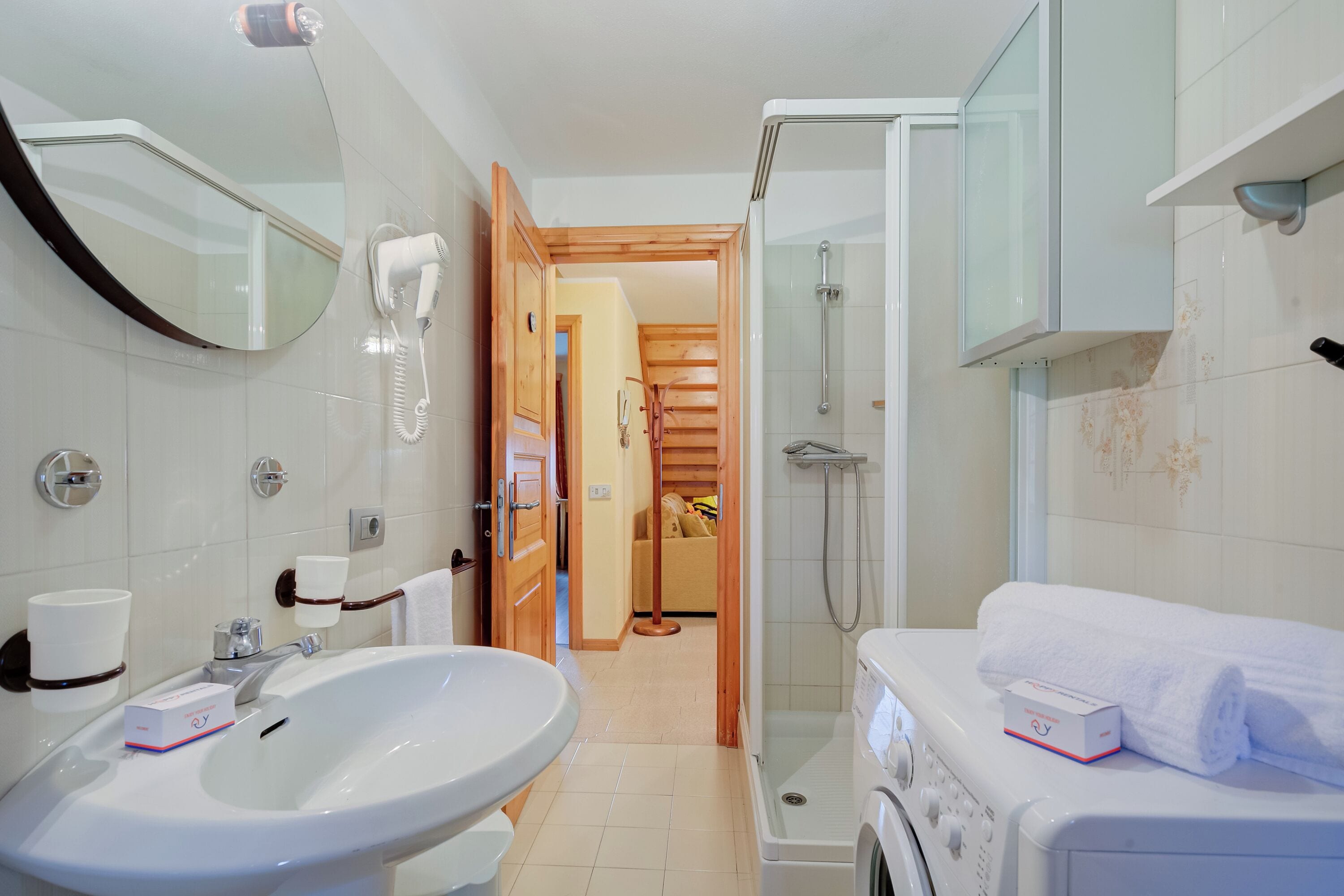 A modern bathroom with a sink, mirror, hairdryer, and a shower area.