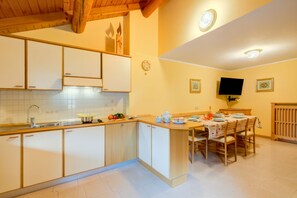 A kitchen with white cabinets, a wooden countertop, a dining table with chairs, and a television mounted on the wall. - Genziana (Livigno)