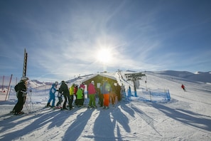 A group of skiers at a ski lift station with a clear sky and sun shining.
