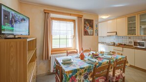 Un comedor con una mesa lista para cuatro, un televisor sobre un mueble de madera y una ventana con cortinas.