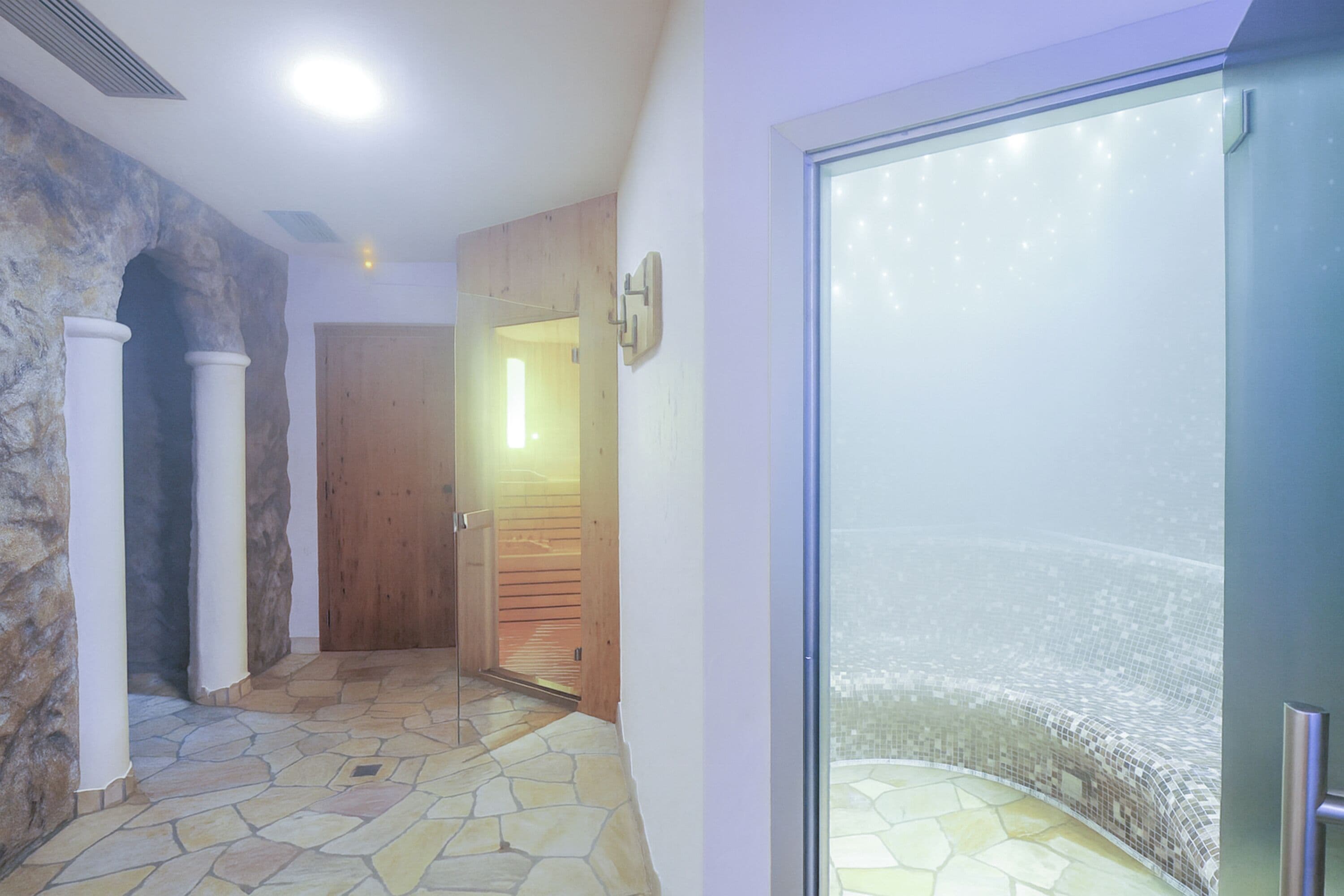 A hallway with stone flooring, a wooden door, and a glass door leading to a balcony with a view.