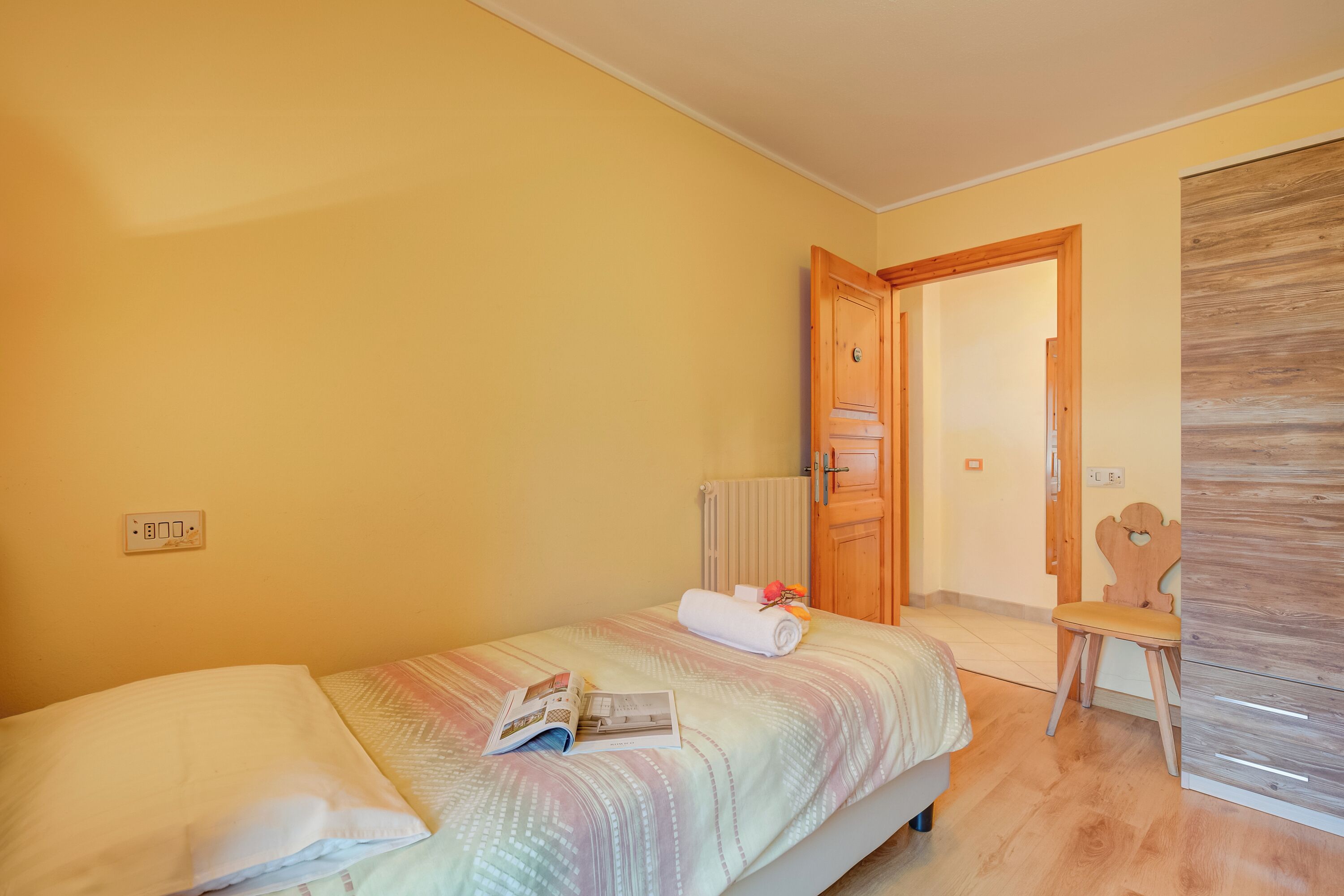 A bedroom with a bed, a chair, a wooden door, and a radiator.