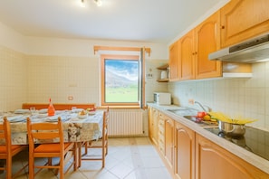 A kitchen with wooden cabinets, a dining table set for four, and a window with a view of a green landscape.