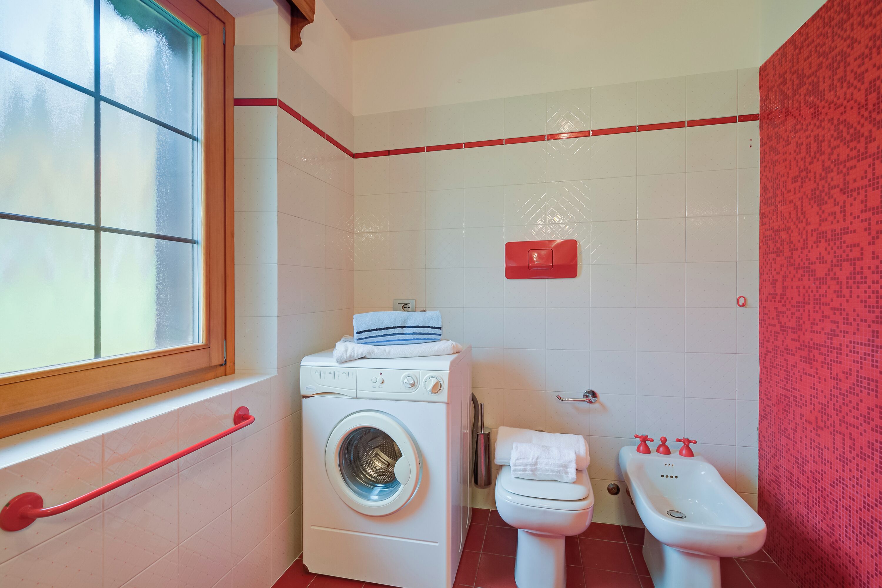 A compact bathroom with a washing machine, toilet, bidet, and a window.