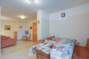 Un coin repas avec une table dressée pour quatre personnes, entourée de chaises en bois. Un téléviseur est fixé au mur, et une porte en bois est visible au fond.