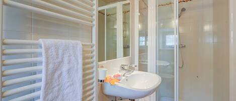 A bathroom with a white sink, a glass shower enclosure, and a towel rack.