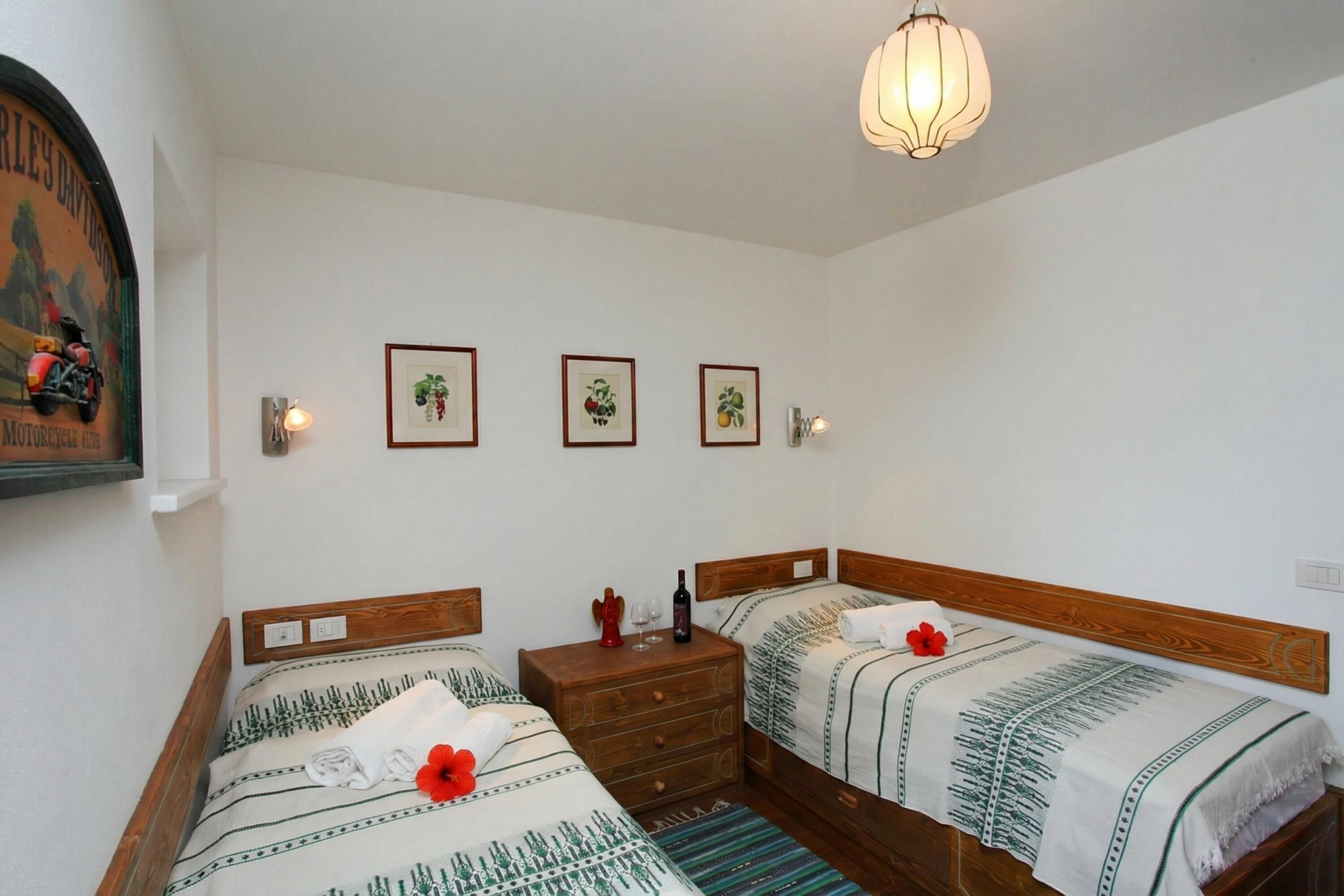 Une chambre avec deux lits, une commode en bois et un luminaire suspendu.