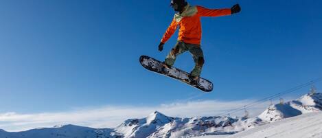 Un snowboarder en pleno vuelo contra un cielo azul despejado.