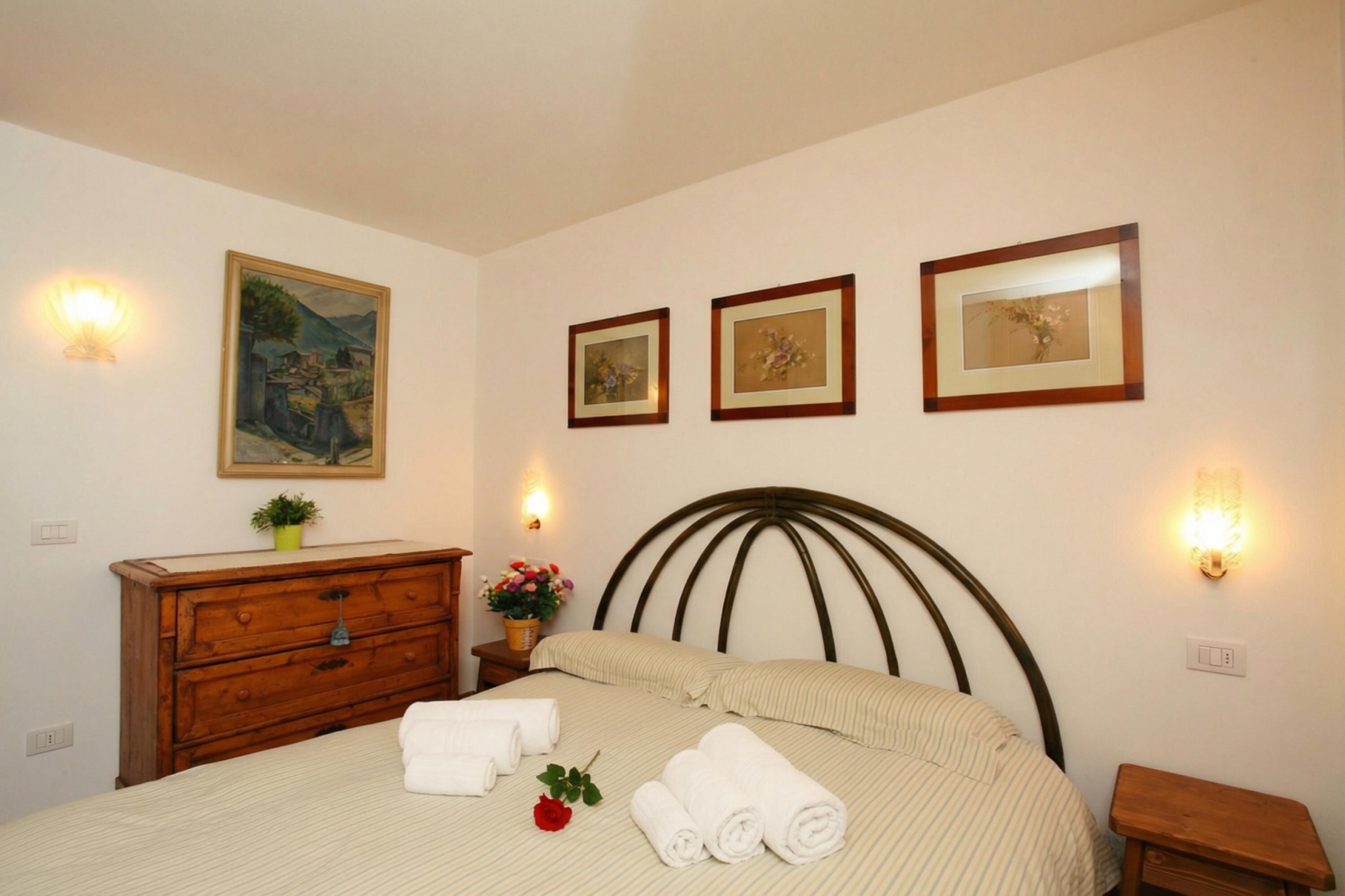 Un dormitorio ordenado con cama, cómoda de madera e iluminación en la pared.