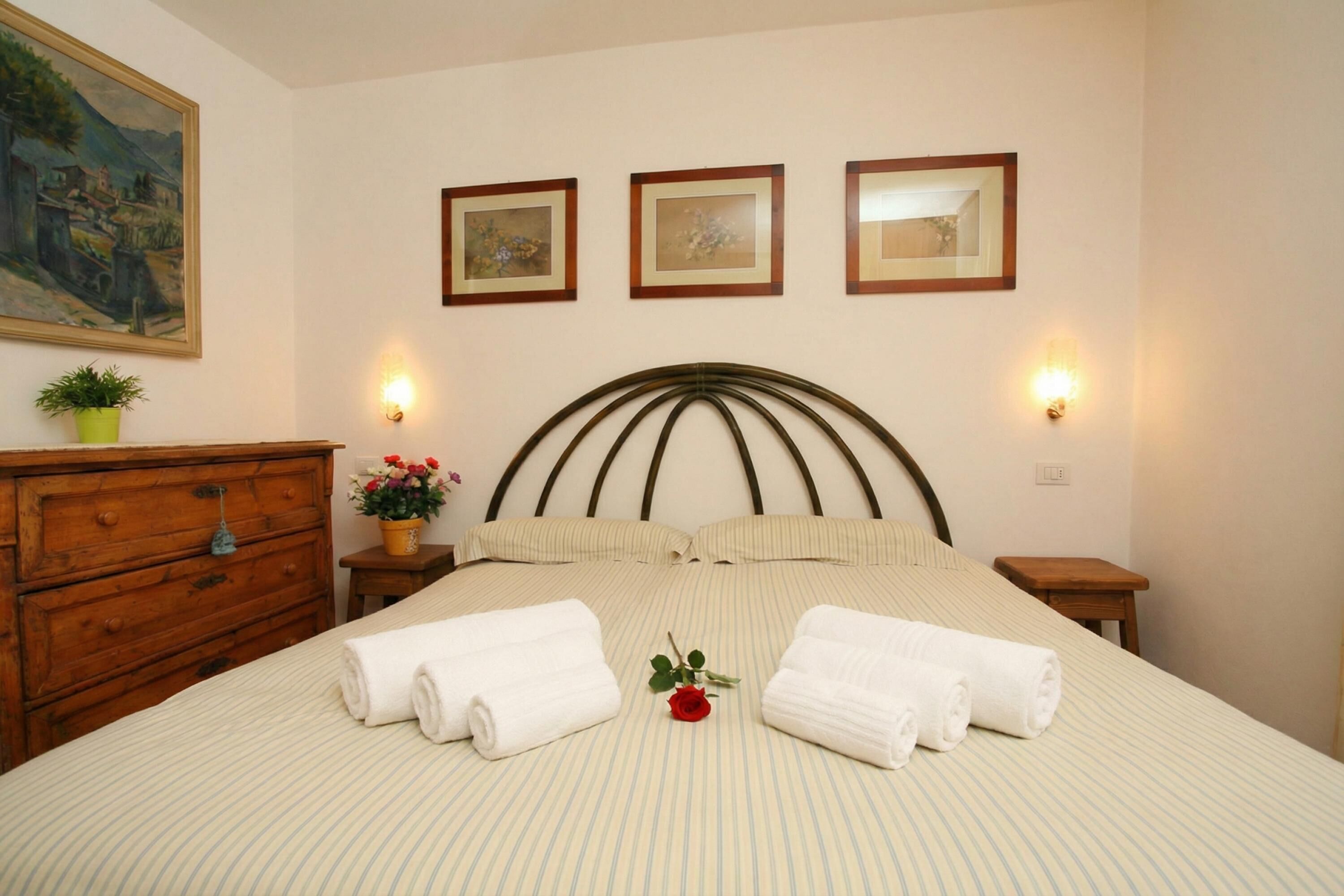A neatly made bed with striped bedding, two bedside tables with lamps, a wooden dresser, and three framed pictures on the wall.