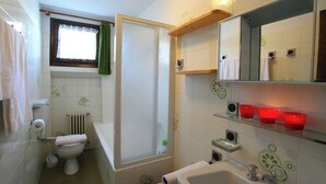 A bathroom with a toilet, bathtub, shower, and a shelf with red glasses. - Vista Livigno (Livigno)