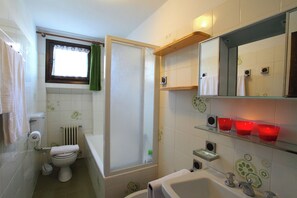 Un bagno con WC, vasca, doccia e uno scaffale con bicchieri rossi.