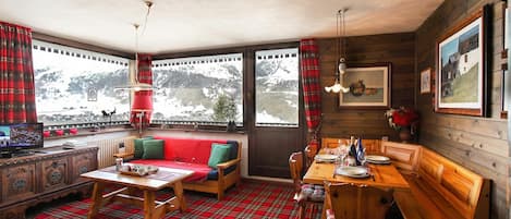 A cozy room with a red plaid carpet, wooden furniture, a dining table set for two, and a large window with curtains.