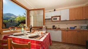 A kitchen with a dining table set for two, a microwave, cabinets, and a view of mountains through a window. - Italia 2 Ski in-Ski out 50m (Livigno)