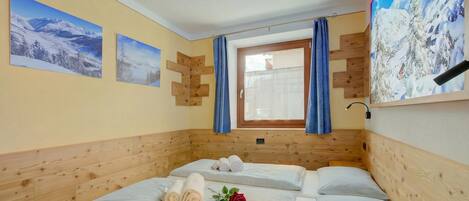 A room with two beds, wooden paneling, a window with curtains, and winter-themed wall art.