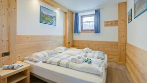 A wooden-paneled room with a bed, a small table, a window with curtains, and a wall-mounted hook. - Italia 2 Ski in-Ski out 50m (Livigno)