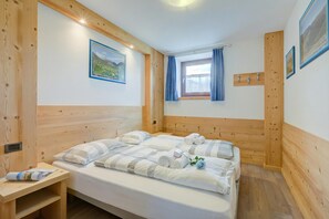 Una habitación con paneles de madera, una cama, una mesita, una ventana con cortinas y un gancho en la pared.