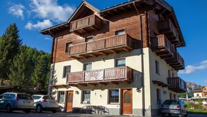 A multi-story wooden building with balconies, parked cars, and a clear sky. - Italia 2 Ski in-Ski out 50m (Livigno)