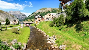 A mountain village with a stream running through it, houses with balconies, and a bridge in the background. - Italia 2 Ski in-Ski out 50m (Livigno)