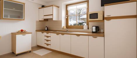 A kitchen with white cabinets, a window, a microwave, and a kettle.