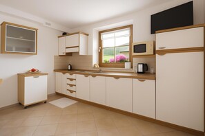 A kitchen with a window, cabinets, a microwave, and a small refrigerator.