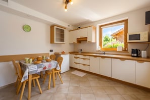A kitchen with a dining table, chairs, cabinets, a window with a view, and a clock on the wall. - Italia 1 Ski in- Ski out 50m (Livigno)
