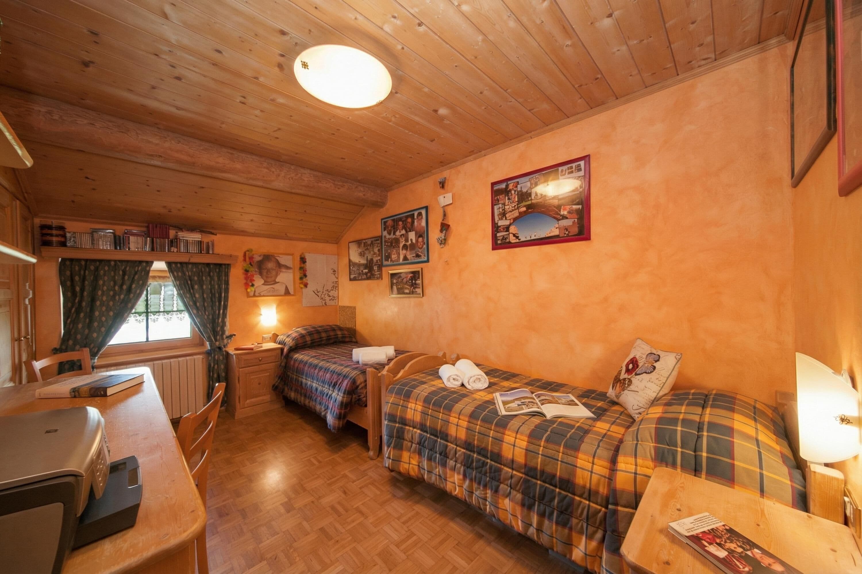 Una habitación acogedora con techos de madera, dos camas con ropa de cama de cuadros, un escritorio con computadora y una ventana con cortinas.