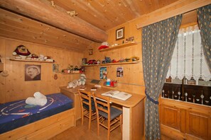 En træhytte med seng, skrivebord, stole, en reol med legetøj og et vindue med gardiner.