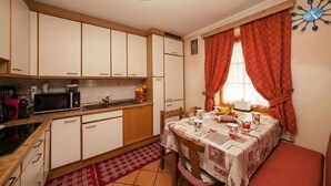 A compact kitchen with white cabinets, a microwave, a sink, and a dining table set with a tablecloth.