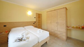 A bedroom with a wooden bed, a wardrobe, and a bedside table with a magazine. - Sole Ski in- Ski out 50m (Livigno)