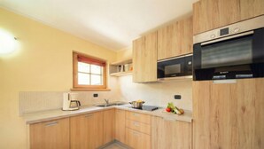 A modern kitchen with wooden cabinets, a built-in oven, and a window with red curtains. - Sole Ski in- Ski out 50m (Livigno)