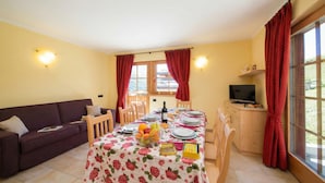 A dining area with a table set for two, a sofa, a TV, and a window with curtains. - Sole Ski in- Ski out 50m (Livigno)