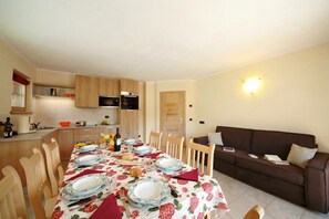 A dining area with a table set for four, wooden chairs, a brown sofa, and a kitchen in the background. - Sole Ski in- Ski out 50m (Livigno)