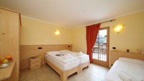 A hotel room with a wooden headboard, two beds, a small bedside table with a magazine, a fruit bowl, and a view of the outdoors through a window with curtains. - Sole Ski in- Ski out 50m (Livigno)