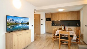 A modern kitchen with wooden cabinets, a dining table set for four, and a flat-screen TV mounted on a wooden cabinet.