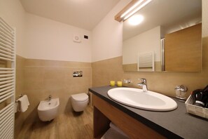 A bathroom with a bidet, toilet, sink, mirror, and towel rack.