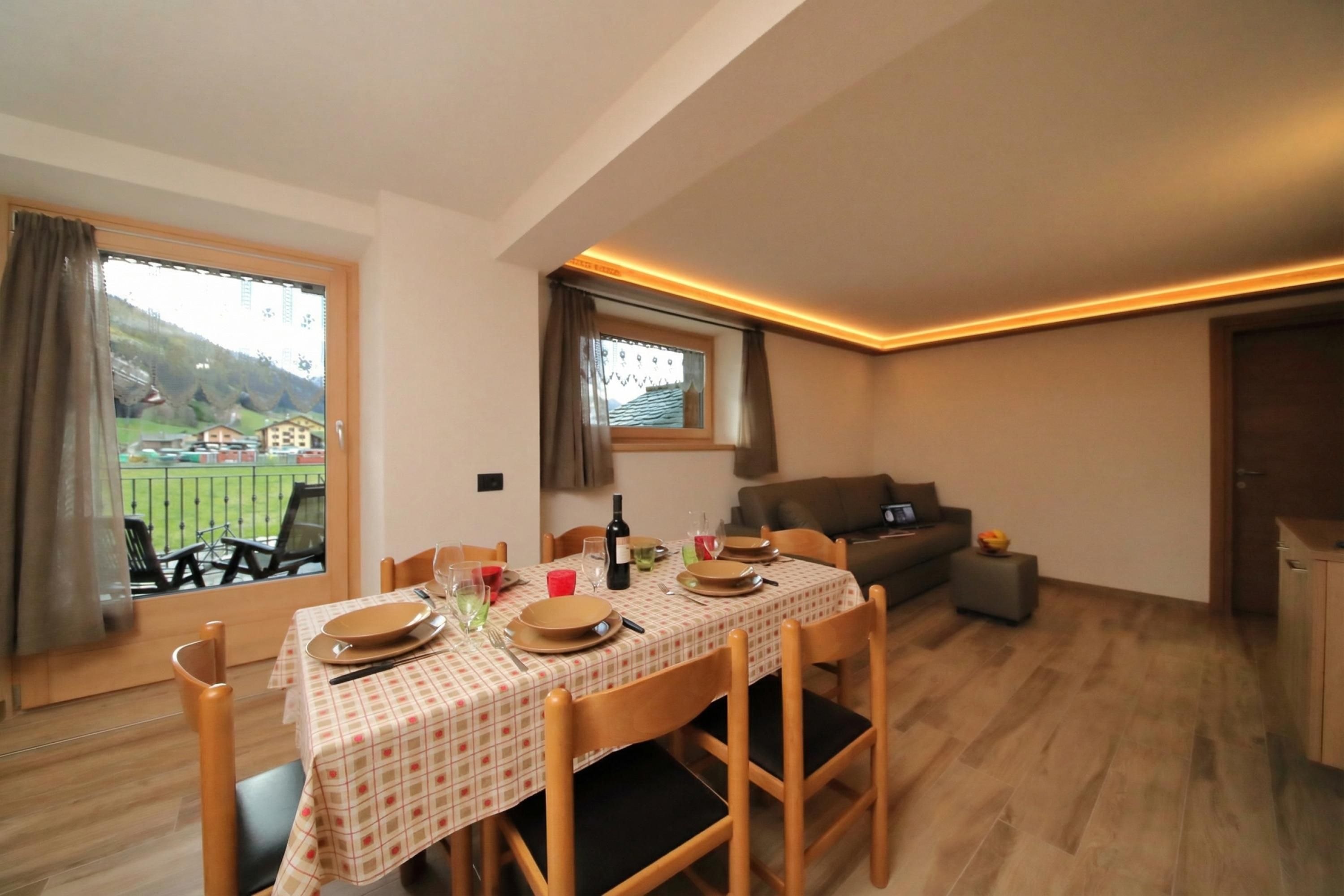 Un coin repas avec une table dressée pour quatre personnes, un canapé et une vue sur un paysage verdoyant.
