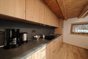 A modern kitchen with wooden cabinets, a black countertop, a coffee maker, a kettle, and a sink. - Reno (Livigno)