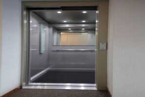 An elevator with a metallic frame, glass panels, and a carpeted floor. - Reno (Livigno)