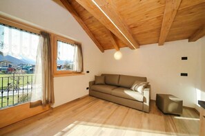 Une pièce avec un plafond en bois, un canapé, un petit pouf et une grande fenêtre avec des rideaux.