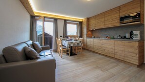 A modern kitchen with wooden cabinets, a dining table with chairs, and a sofa in a living area.