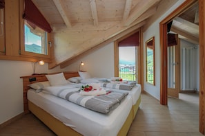 A bedroom with two beds, wooden ceiling beams, and a view of a green landscape.