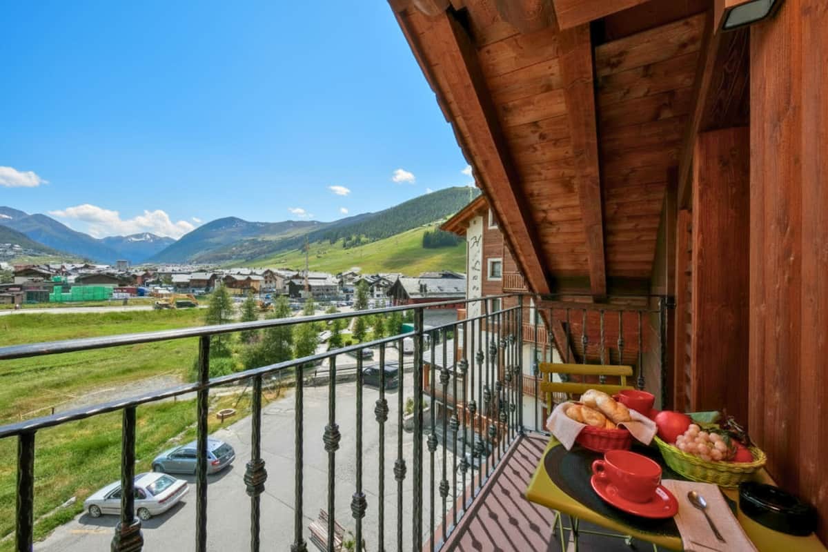 A balcony with a table set for breakfast, overlooking a mountainous landscape with buildings in the distance.