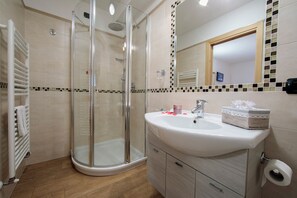 A bathroom with a glass-enclosed shower, a sink with toiletries, and a mirror.