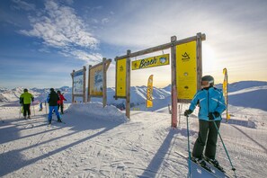 A ski slope with wooden signage and flags, surrounded by snow-covered mountains. - Tamigi (Livigno)