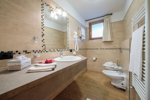 A modern bathroom with a large mirror, a sink, a bidet, and a window with a curtain. - Tamigi (Livigno)