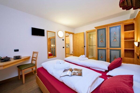 A hotel room with two beds, a desk with a chair, a TV, a mirror, and a wardrobe. - Tamigi (Livigno)